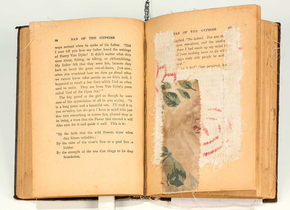 A yellowed book propped open with fabric and paint covering the right page.