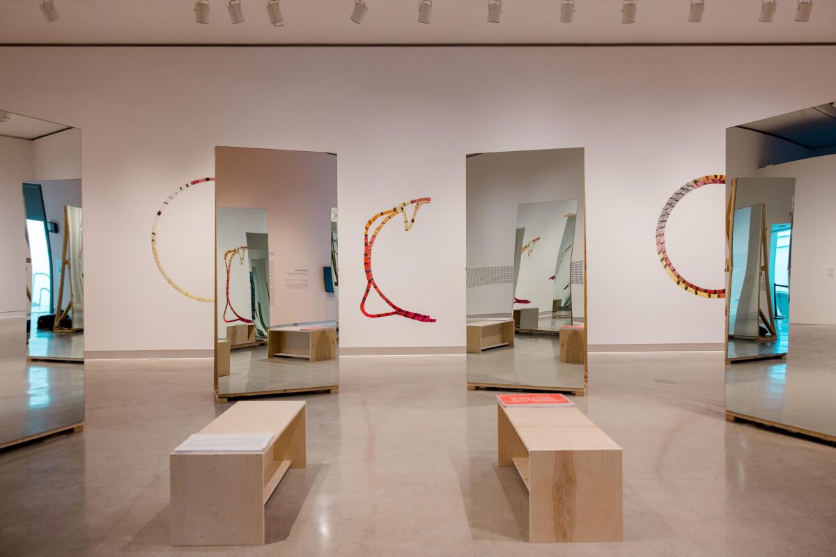 A gallery space with three large mirrors and benches.